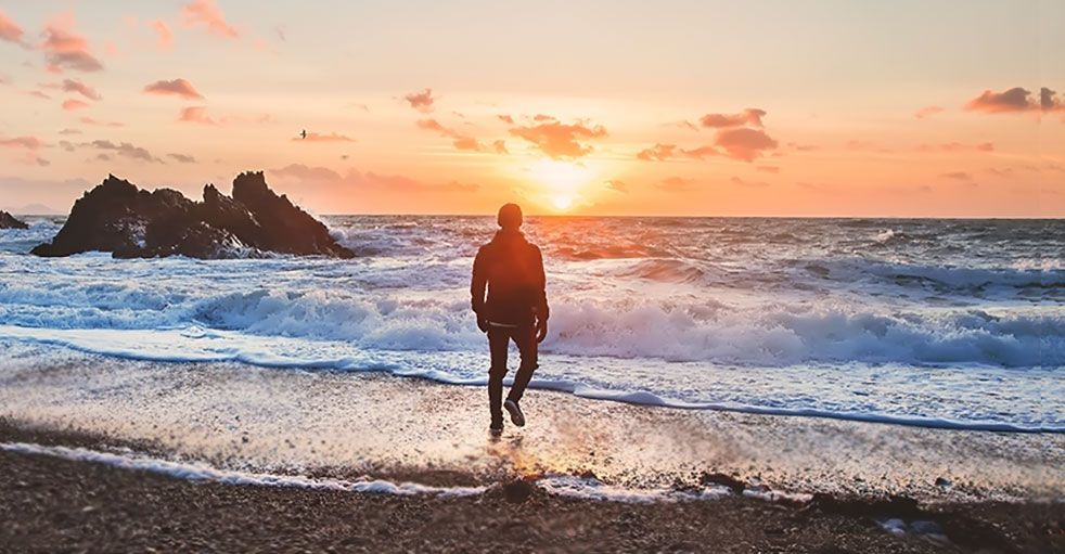 Man on beach walking toward sunrise