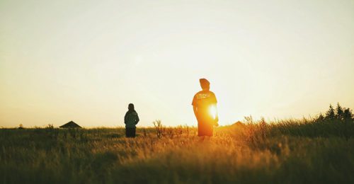 two people in a field as the sun sets