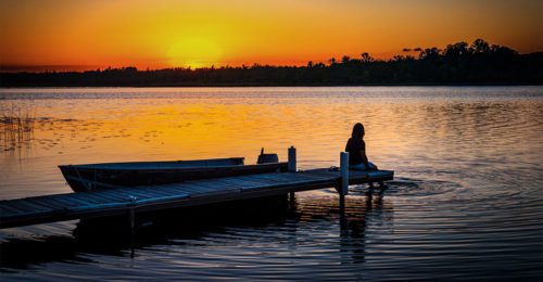 Woman sitting on dock looking at sunset