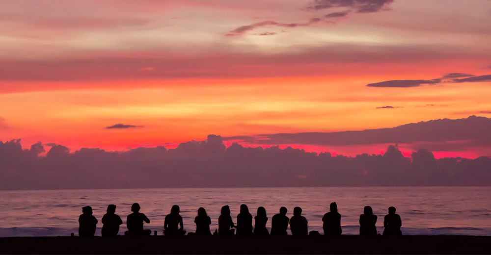 group of people sitting on beach watching sunset
