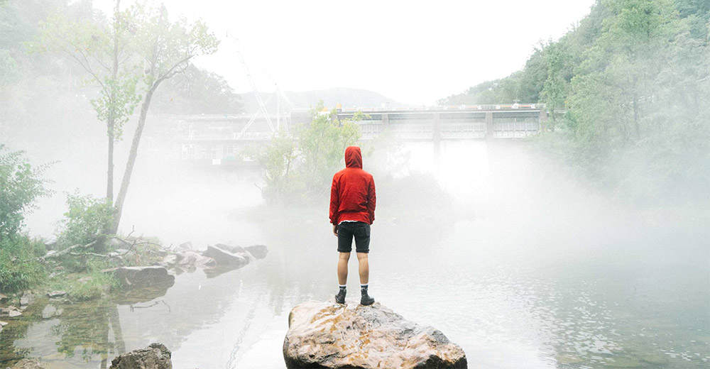 Man standing on river rock looking at river
